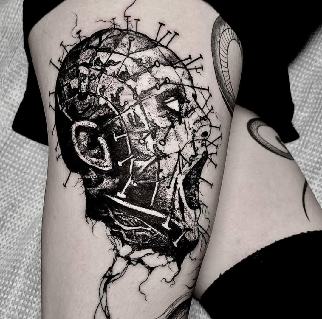 Blackwork and dotwork tattoo of a pin-studded head on a thigh